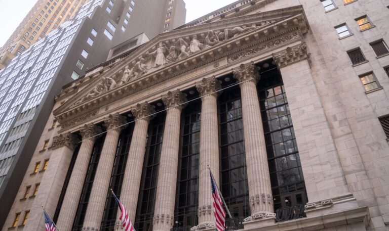 New York Stock Exchange building facade and American flags on Wall Street.
