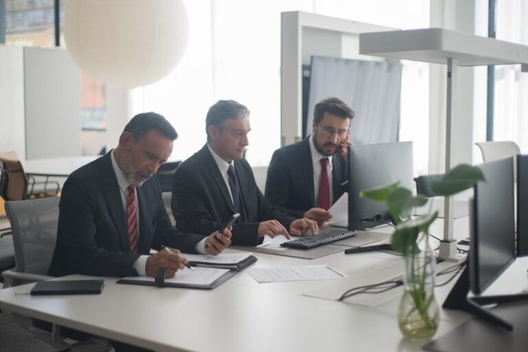Three office professionals reviewing documents and computer screens at work