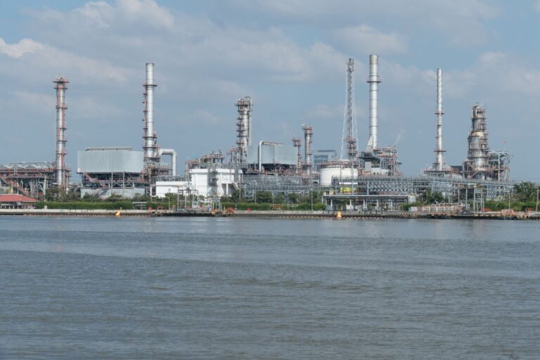 Oil refinery towers and pipework beside a waterfront under a cloudy sky