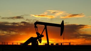 An oil pump jack in silhouette against an orange sunset sky